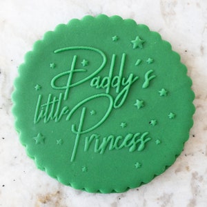 Puede incluir: Galletas redondas verdes con glaseado blanco y el texto "Paddy's little Princess" con pequeñas estrellas blancas.