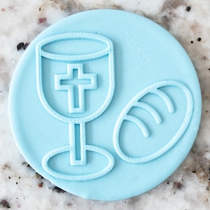 May include: A light blue cookie cutter featuring a chalice and a loaf of bread. The chalice has a cross on the front.