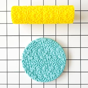 Könnte beinhalten: Zwei Silikon-Nudelhölzer zum Backen, eines gelb und eines blau. Beide haben ein dekoratives Blumenmuster.