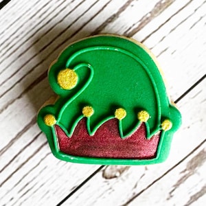 Puede incluir: Galletas de Navidad verdes y rojas decoradas como un gorro de elfo con detalles dorados.