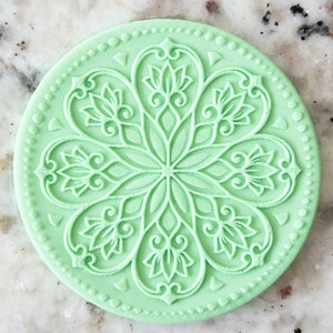May include: A light green round silicone mold with a detailed, intricate, floral design. The mold is perfect for creating decorative cakes, cookies, or other baked goods.