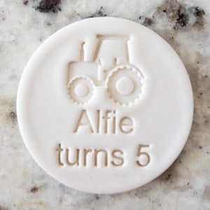 Puede incluir: Sello de arcilla redondo blanco con un diseño de tractor y el texto "Alfie turns 5".