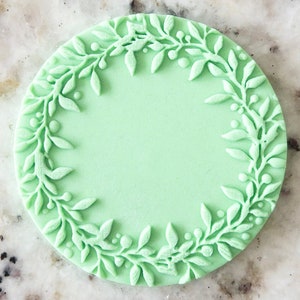 Op de afbeelding: Een ronde cakedecoratiestempel in lichtgroen met een gedetailleerd bloemmotief rond de rand.