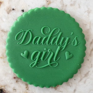 Puede incluir: Galletas redondas verdes con el texto "Daddy's girl" en letras blancas en cursiva y dos pequeños corazones blancos a cada lado del texto.