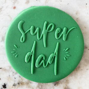 Puede incluir: Una galleta redonda verde con las palabras "super papá" en relieve.