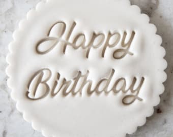 Könnte beinhalten: Ein weißer, kreisförmiger Fondantstempel mit gewelltem Rand. Die Worte "Happy Birthday" sind elegant in einer Schreibschrift in die Mitte geschnitzt und erzeugen einen dekorativen Eindruck für Kuchen und Backwaren.