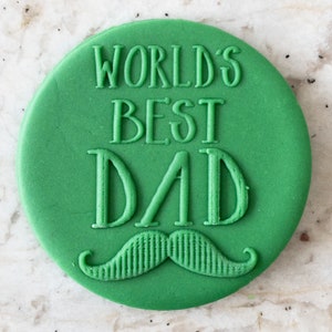 Puede incluir: Galletas redondas verdes con las palabras "World's Best Dad" y un bigote verde.