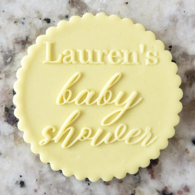 May include: A yellow round cake topper with the text "Lauren's baby shower" in white.