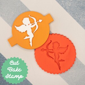 May include: A set of two cookie cutters, one orange and one red, shaped like a cupid with wings and an arrow. The cutters are labeled "Cut Bake Stamp".