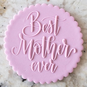 May include: A pink round cookie with scalloped edges and the text "Best Mother Ever" written in cursive.