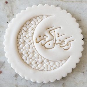 May include: White fondant cookie cutter with a crescent moon and Arabic calligraphy that reads "Ramadan Kareem".
