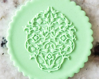Puede incluir: Un adorno redondo para pastel de color verde claro con un diseño floral blanco intrincado.