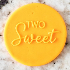 Può includere: Un tagliapasta rotondo di colore giallo brillante con le parole "TWO Sweet" in rilievo al centro.