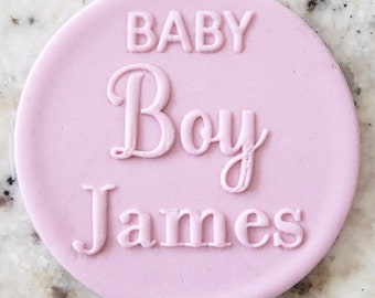 Könnte beinhalten: Runder Fondant-Stempel in Rosa mit dem Text "BABY Boy James" in Weiß.