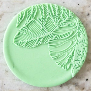 May include: A light green round cake topper with a white embossed leaf design.