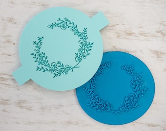Puede incluir: Dos plantillas redondas para pasteles, una azul claro y otra azul, con un diseño de corona de flores.