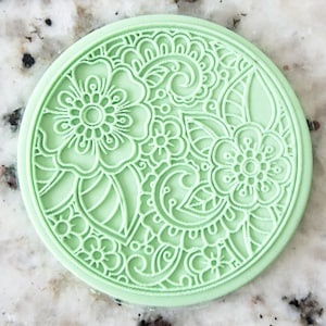 May include: A round, green silicone stamp with a detailed floral design. The design features intricate swirls, leaves, and flowers.