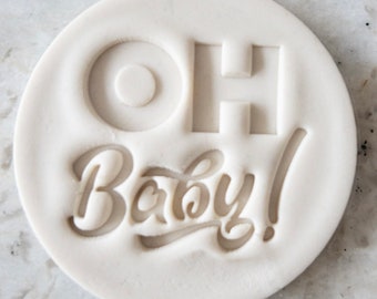 Puede incluir: Estampador de horneado de silicona blanco con las palabras "Oh Baby!" en una fuente cursiva.