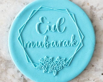 May include: A light blue round stamp with a geometric frame and the text "Eid Mubarak" in a cursive font. The frame is decorated with a floral design at the bottom.