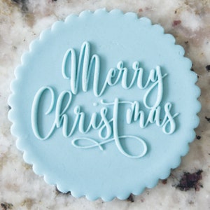 May include: A light blue round cake topper with the words "Merry Christmas" written in white cursive script.
