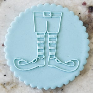 May include: A light blue fondant cookie with an embossed design of an elf's legs and shoes.