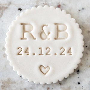 May include: White round ceramic stamp with the initials "R&B" and the date "24.12.24" in a serif font. A small heart is below the date.