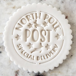 May include: White round cookie cutter with a scalloped edge. The cutter is embossed with the words "North Pole Post Special Delivery" and five stars.