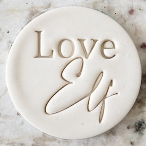 May include: White round cookie cutter with the words "Love Elf" embossed in the surface.