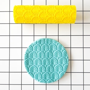Puede incluir: Un rodillo amarillo con un patrón repetitivo de formas de abanico superpuestas. Un rodillo azul turquesa con el mismo patrón se muestra al lado.