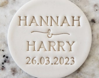 Pode incluir: Azulejo redondo de cerâmica branca com o texto "HANNAH & HARRY 26.03.2023" gravado em cor castanho claro.