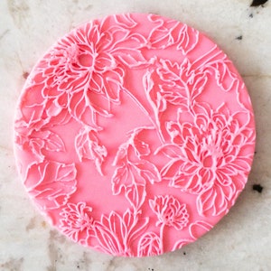 Può includere: Un motivo floreale rotondo rosa con dettagli bianchi in rilievo. Il design presenta grandi fiori e foglie stilizzate, creando una superficie strutturata. L'estetica generale è delicata e decorativa, adatta per l'artigianato o l'arredamento della casa.