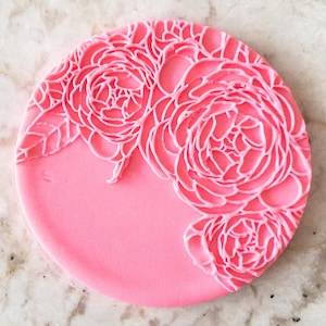 May include: A pink silicone mold with a raised design of two large peonies. The mold is circular and has a smooth surface.