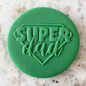 Puede incluir: Cortador de galletas redondo verde con las palabras "SUPER dad" en relieve en forma de superhéroe.