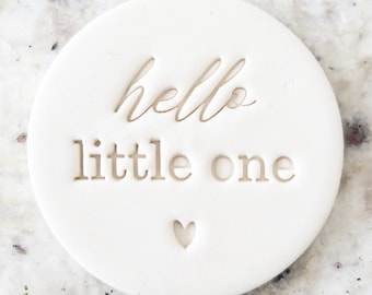 May include: White round ceramic ornament with the text "hello little one" and a small heart.