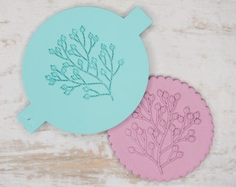 Puede incluir: Dos plantillas redondas para decorar pasteles, una azul claro y otra rosa, con un diseño floral de una rama con pequeñas bayas.