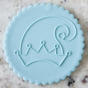 Puede incluir: Una galleta redonda de color azul claro con un contorno blanco de una corona y un diseño de espiral.