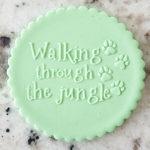 May include: A light green round cookie with the text "Walking through the jungle" and four paw prints.