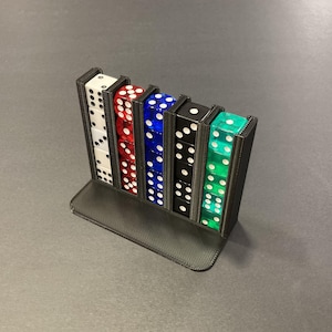 Op de afbeelding: Een dobbelsteenhouder met vijf kolommen, elk met zes dobbelstenen. De dobbelstenen zijn wit, rood, blauw, zwart en groen, met witte ogen. De houder is zwart en staat op een platte basis, geschikt voor tafelspellen.