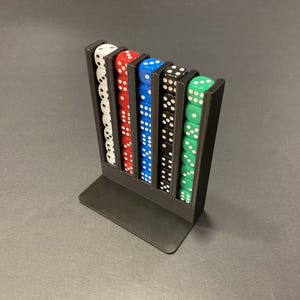 Könnte beinhalten: Ein schwarzer Würfelhalter mit sechs Spalten, die jeweils einen Stapel Würfel halten. Die Würfel sind weiß, rot, blau, schwarz und grün. Die Würfel haben weiße Punkte. Der Halter besteht aus schwarzem Kunststoff und steht auf einer flachen Basis.