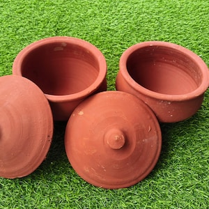 May include: Two terracotta pots with matching lids. Each pot has a wide, open circular mouth and a smooth, reddish-brown finish. The lids are circular with a small, centred knob handle on top. The pots are deep and have a simple, functional design.
