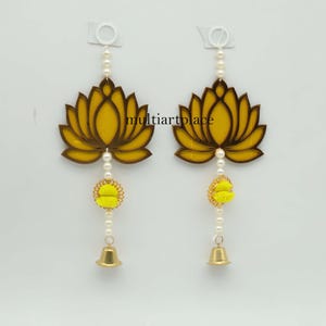 May include: Two decorative lotus flower ornaments. Each ornament features a yellow lotus flower design with brown outlines, a string of pearls, a yellow and gold accent, and a small gold bell. The ornaments hang from white clips.