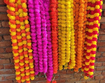 May include: A collection of long, hanging floral garlands made of artificial marigold-style flowers in vibrant shades of yellow, orange, hot pink, and red. The garlands are suspended in vertical rows, with some loose strands pooled at the bottom.