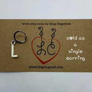May include: Silver charm earring with the letter L hanging from a hoop. The earring is sold as a single earring. The card says "sold as a single earring" and includes the website www.etsy.com/ca/shop/lingechow and email address email.linge@gmail.com.