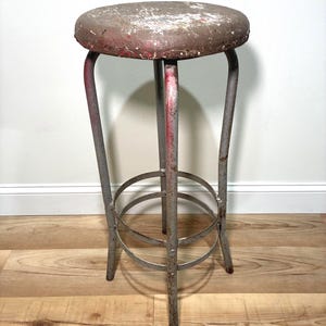 May include: An industrial-style bar stool with a round, distressed seat in shades of red, brown, and white. The stool has a metal frame with a footrest and measures approximately 30 inches in height.