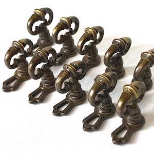 May include: A collection of ten antique bronze-colored drawer pulls. Each pull features a curved handle with a decorative top and a base with a keyhole-shaped opening. The hardware is arranged on a white surface.