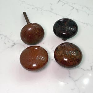 May include: Four antique cabinet knobs in shades of brown. One knob has a metal stem. The knobs have a glossy finish and vary in color and pattern, including a dark brown, a lighter brown, and a patterned brown.