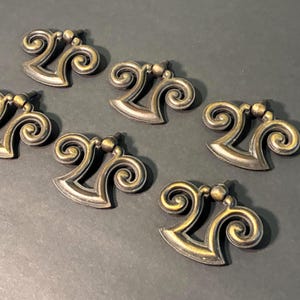 May include: Six antique bronze-toned drawer pulls with a decorative scroll design. Each pull features a stylized shape with a central ball detail. The pulls are arranged on a dark surface.