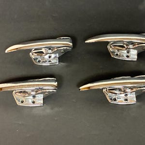 May include: Four chrome-plated door handles with a curved lever design. The handles are mounted on a base with multiple screw holes, and are set against a dark background.