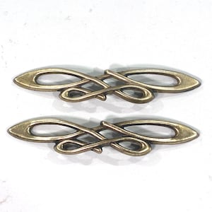 May include: Two antique bronze-colored decorative metal embellishments. Each has an elongated oval shape with an intricate, swirling design in the center. The metal has a slightly aged, vintage appearance.