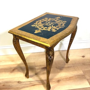 May include: An antique side table with a rectangular top featuring a dark teal surface and gold ornate design. The table has a gold-painted frame and legs with a curved design, adding a touch of elegance to any room.